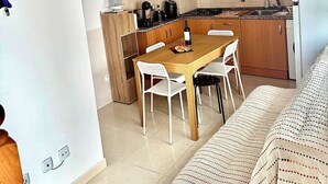 A compact kitchen with wooden cabinets, a dining table with chairs, and a refrigerator.