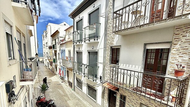 A narrow cobblestone street lined with multi-story buildings, each with balconies and windows.