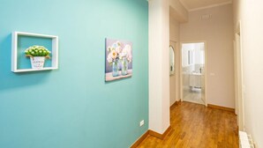Un pasillo con una pared verde azulada, suelo de madera, una obra de arte enmarcada y un pequeño estante con una planta en maceta.
