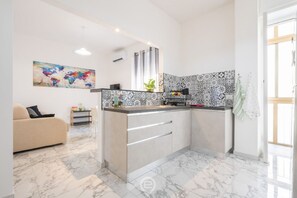 A modern kitchen with a marble floor, a built-in island with drawers, a patterned backsplash, and a large abstract painting on the wall.