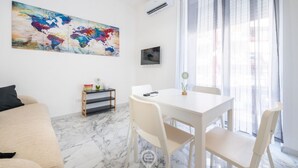 Un salon moderne avec un canapé blanc, une table à manger avec des chaises, un tableau représentant une carte du monde et une petite étagère ornée d’objets décoratifs.