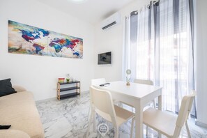 Ein modernes Wohnzimmer mit einem weißen Sofa, einem Esstisch mit Stühlen, einem Wandbild mit einer Weltkarte und einer kleinen Regal mit Dekorationselementen.