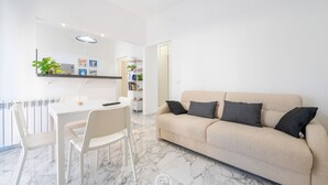 Un salon moderne avec un canapé beige, une table à manger avec des chaises et, au fond, un coin cuisine.