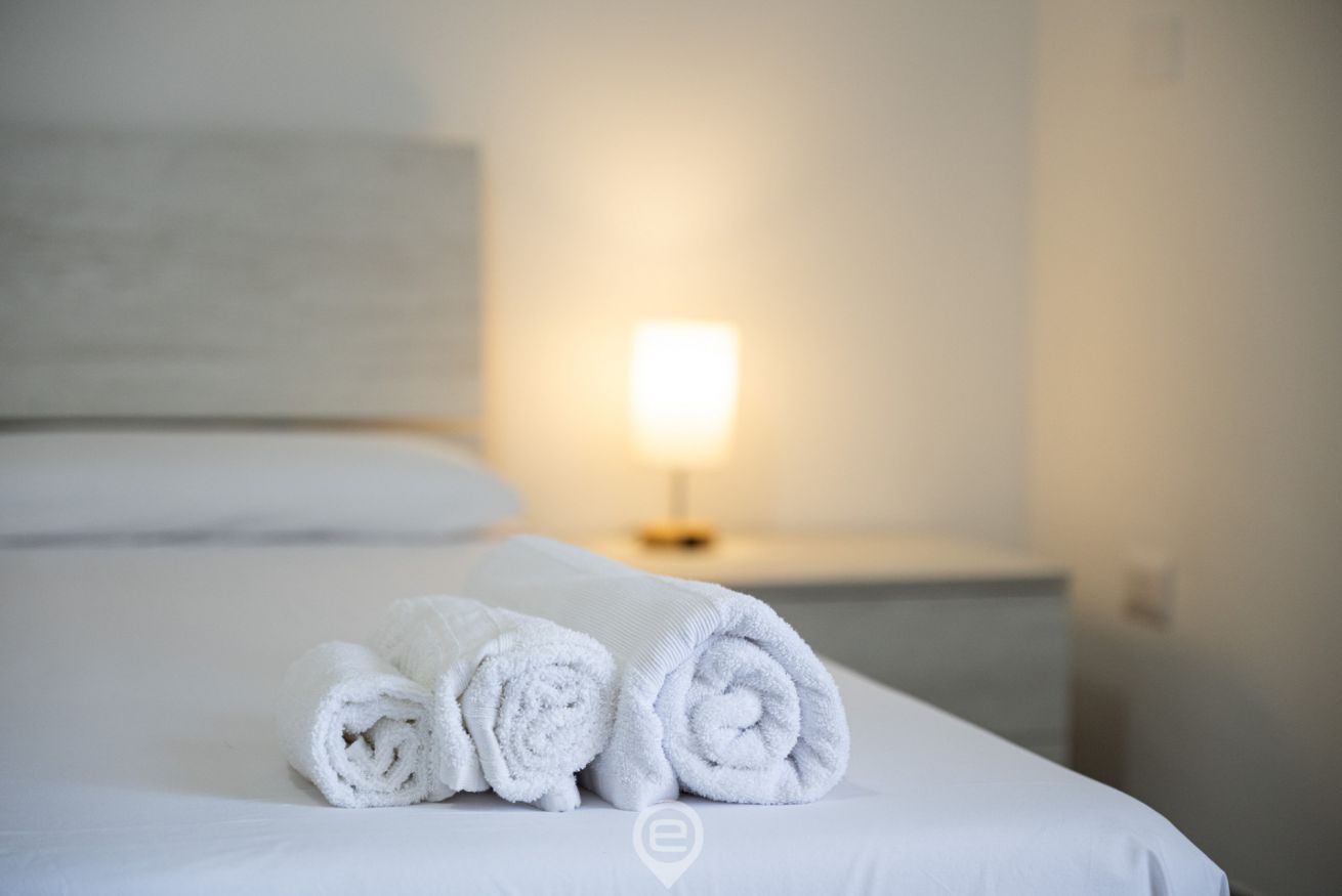 A neatly made bed with rolled white towels and a bedside lamp.