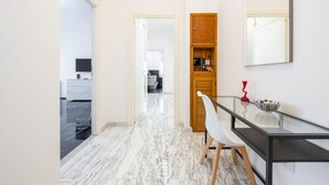 Un couloir moderne avec un sol en marbre, une table en verre avec une chaise et un meuble en bois doté d’un miroir.
