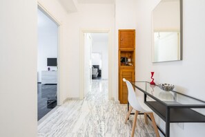 Ein moderner Flur mit Marmorboden, einem Glastisch mit einem Stuhl und einem Holzschrank mit Spiegel.