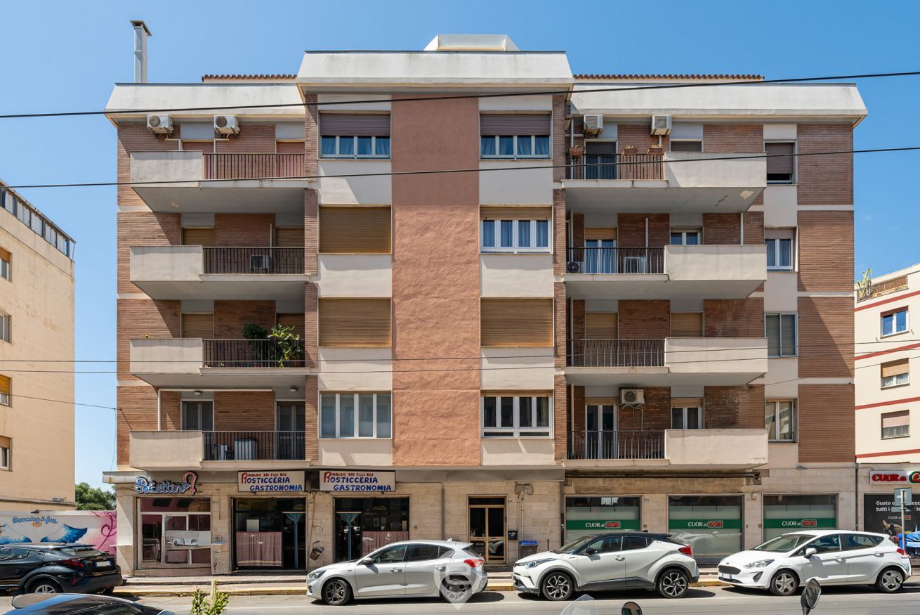 A multi-story building with balconies, a storefront with a sign reading "Postegceria Gastronomia," and several parked cars.