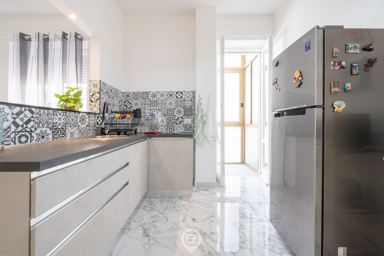 A modern kitchen with a patterned backsplash, a stainless steel refrigerator, and a marble floor.