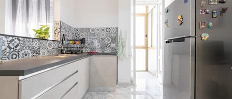 A modern kitchen with a patterned backsplash, a stainless steel refrigerator, and a marble floor.