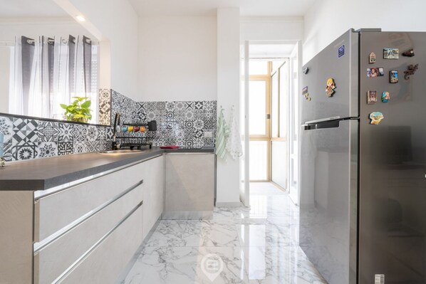 A modern kitchen with a patterned backsplash, a stainless steel refrigerator, and a marble floor.
