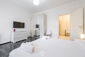 A modern hotel room with a large bed, a flat-screen TV, a wardrobe, and a bathroom visible through an open door.