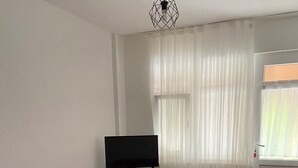 Een kamer met een rode bank, een televisie, een tafeltje en een raam met gordijnen.