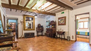 Amplia habitación con techo alto, vigas de madera y suelo de baldosas. Se observa un espejo grande, un mueble de madera y una pequeña mesa con una lámpara.