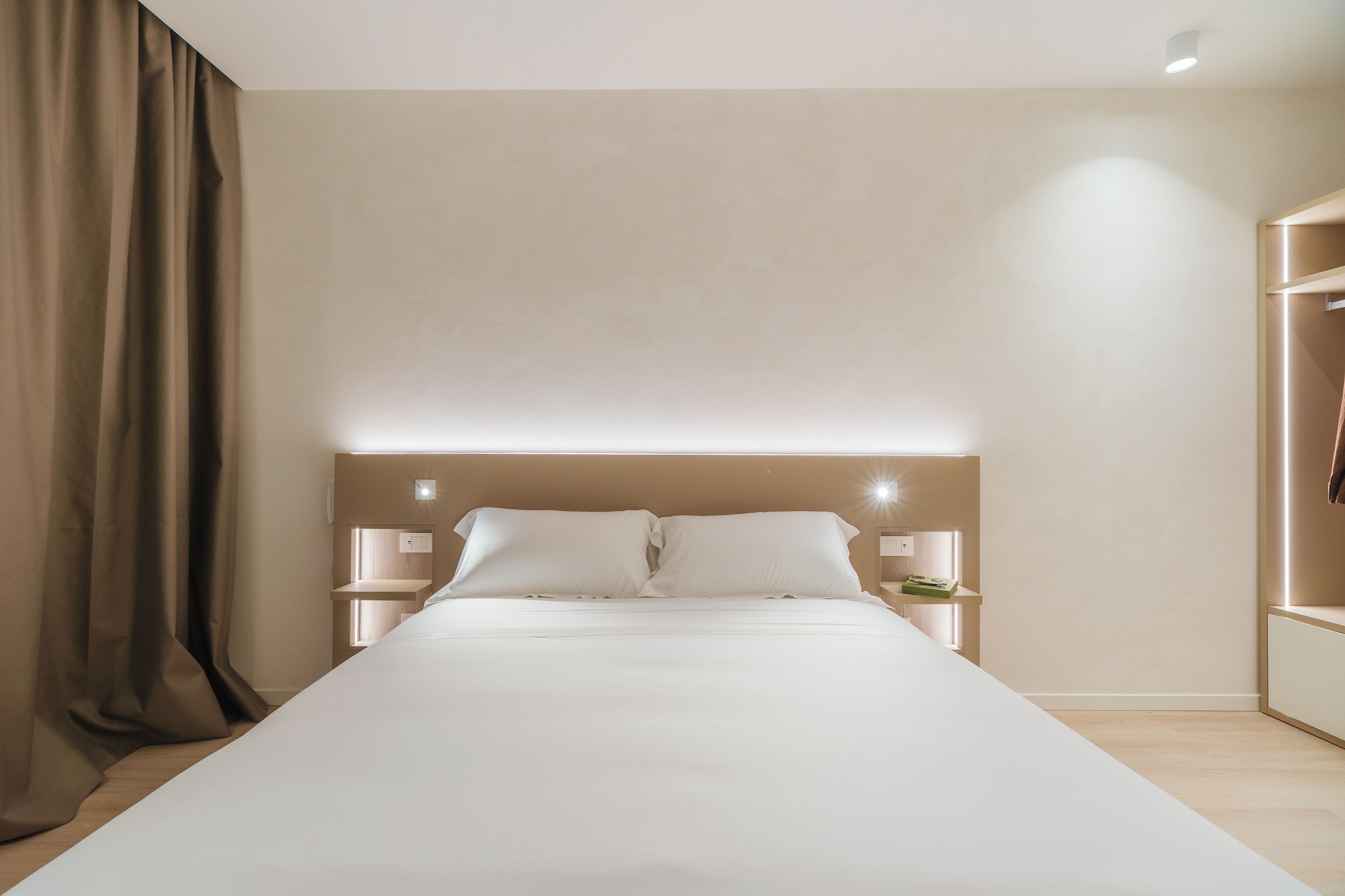 Quarto de hotel moderno com uma cama grande, mesas de cabeceira e um guarda-roupa embutido.