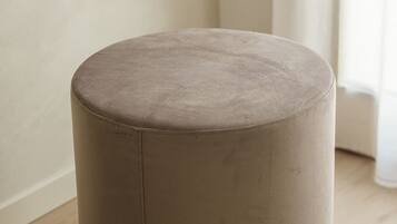 Een rond, beige poef in een kamer met een houten vloer en een witte muur.
