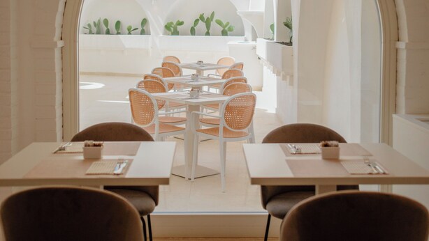 A dining area with white tables and chairs, an arched doorway leading to an outdoor patio with plants. - Maison Sirolo (Sirolo)