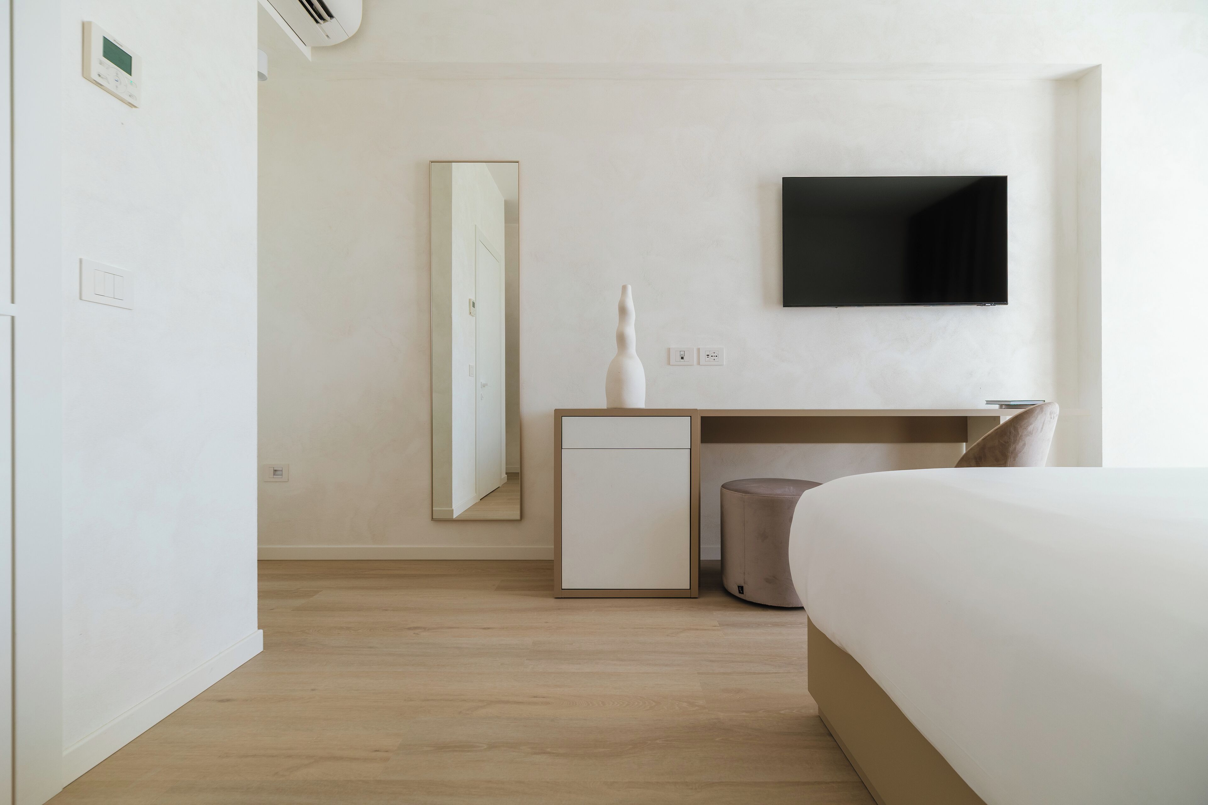 Camera d'albergo con un letto, una scrivania con sedia, un piccolo frigorifero, uno specchio e un televisore a schermo piatto montato a parete.