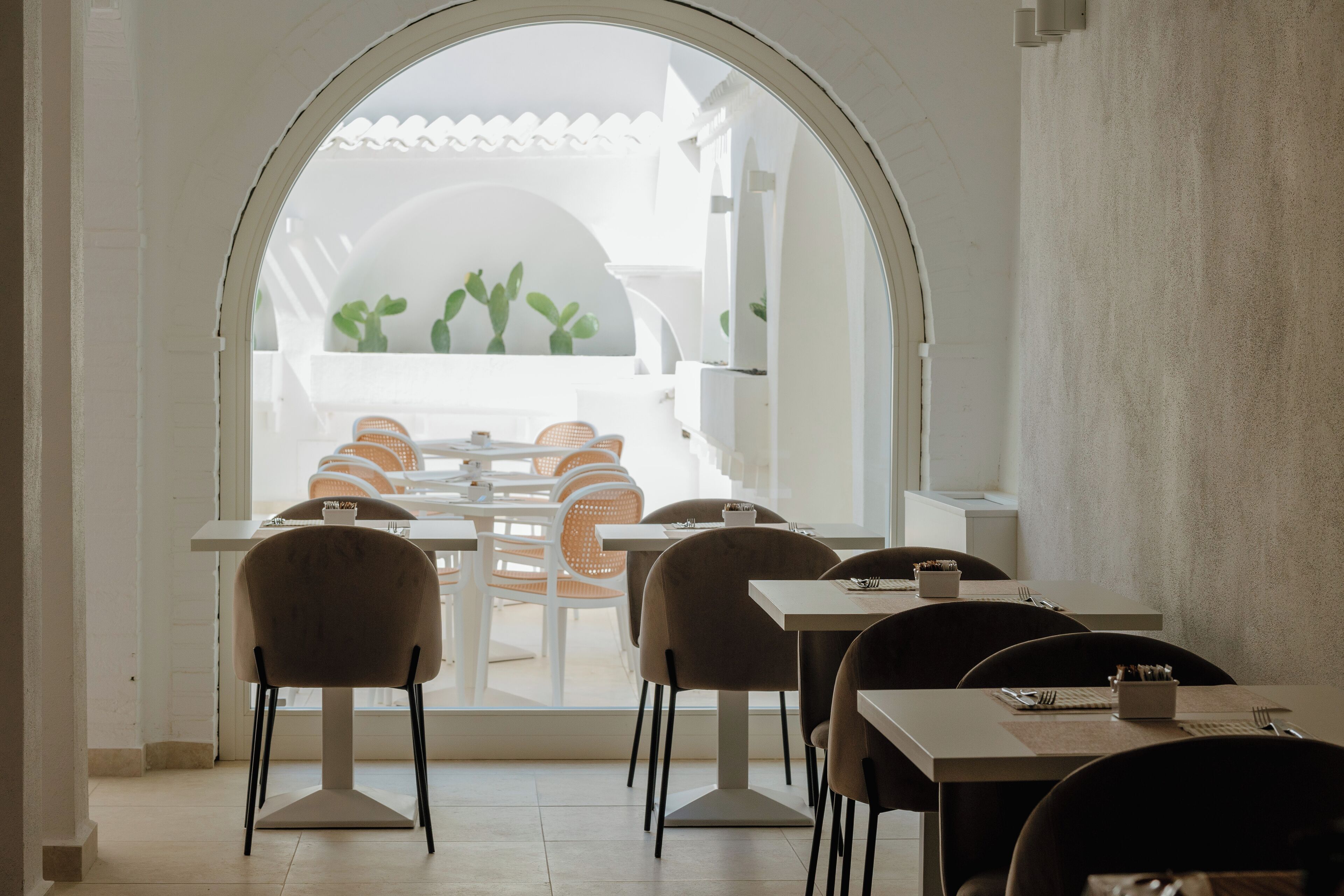 A dining area with tables and chairs, an arched doorway leading to a patio with plants.