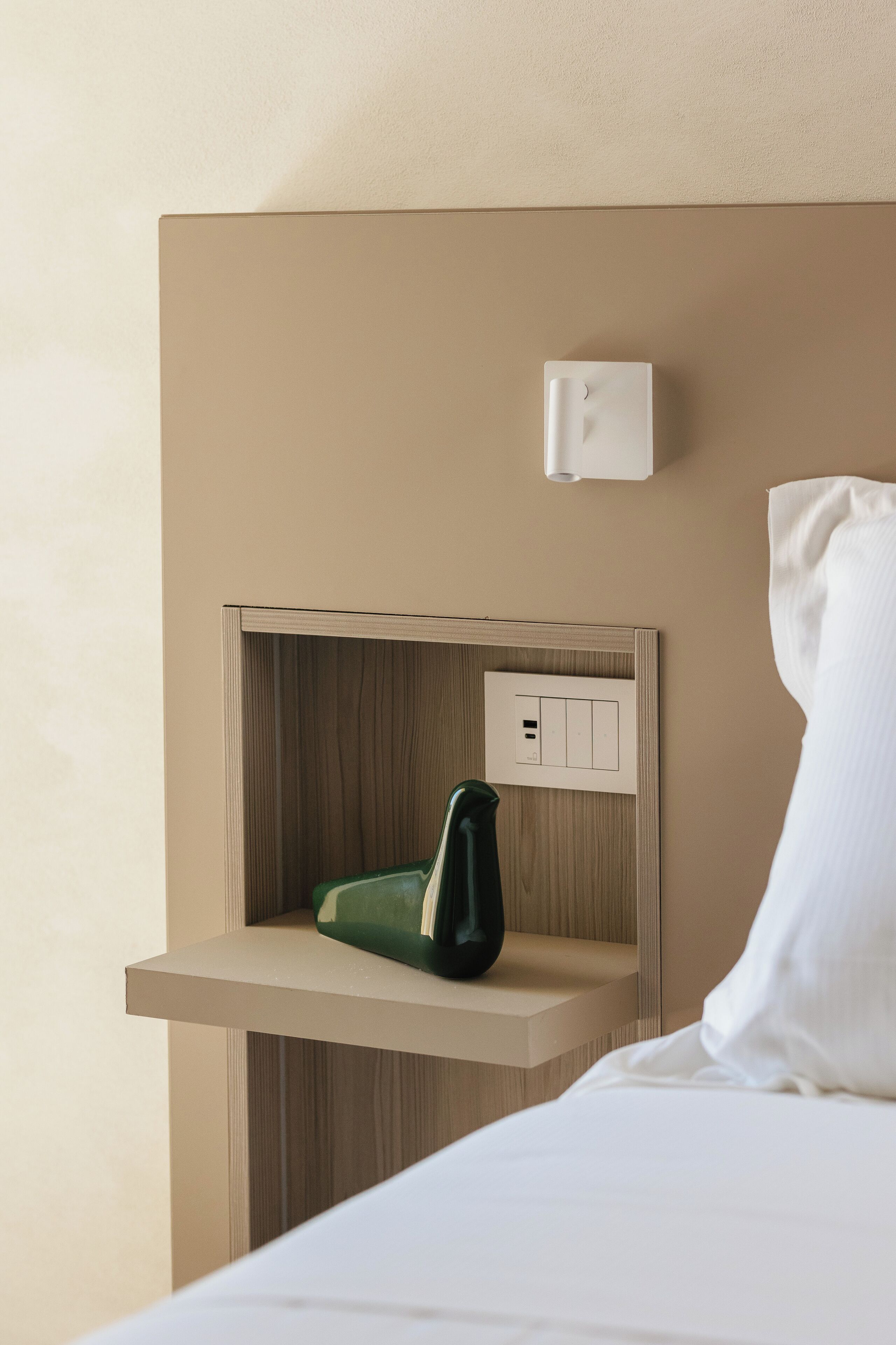 Habitació d'hotel amb un llit, una taula de nit, una presa elèctrica i un interruptor a la paret.
