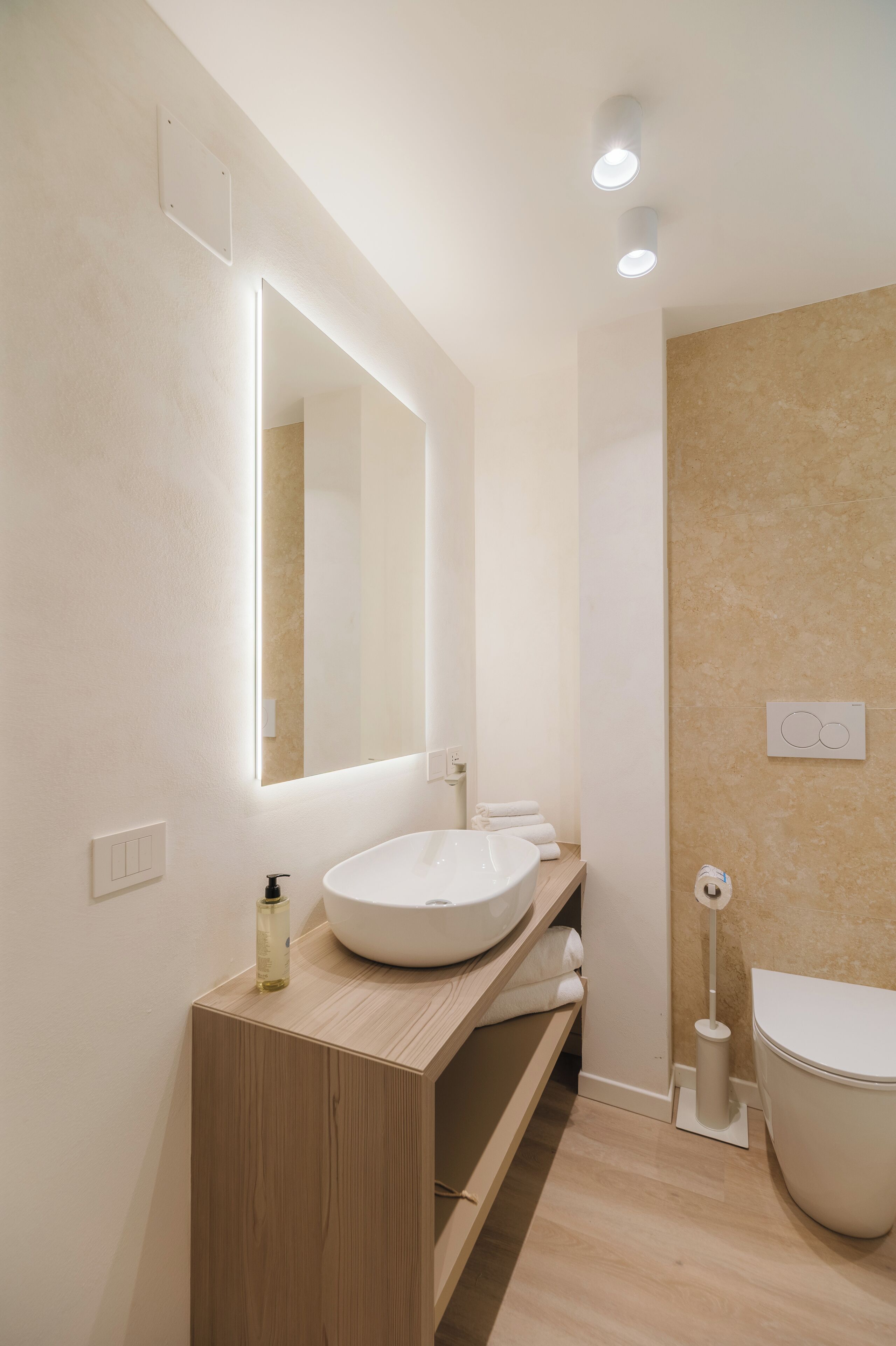 Een moderne badkamer met een houten wastafelmeubel, een witte wastafel, een grote spiegel en een toilet.