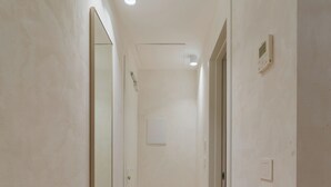 A narrow hallway with light-colored walls and wooden flooring. There are two doors on the right side and a large mirror on the left. - Maison Sirolo (Sirolo)