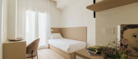 A modern hotel room with a bed, a desk, a chair, and a small table with flowers.
