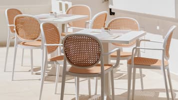 An outdoor patio with white tables and chairs, a white wall with a decorative cornice, and potted cacti.