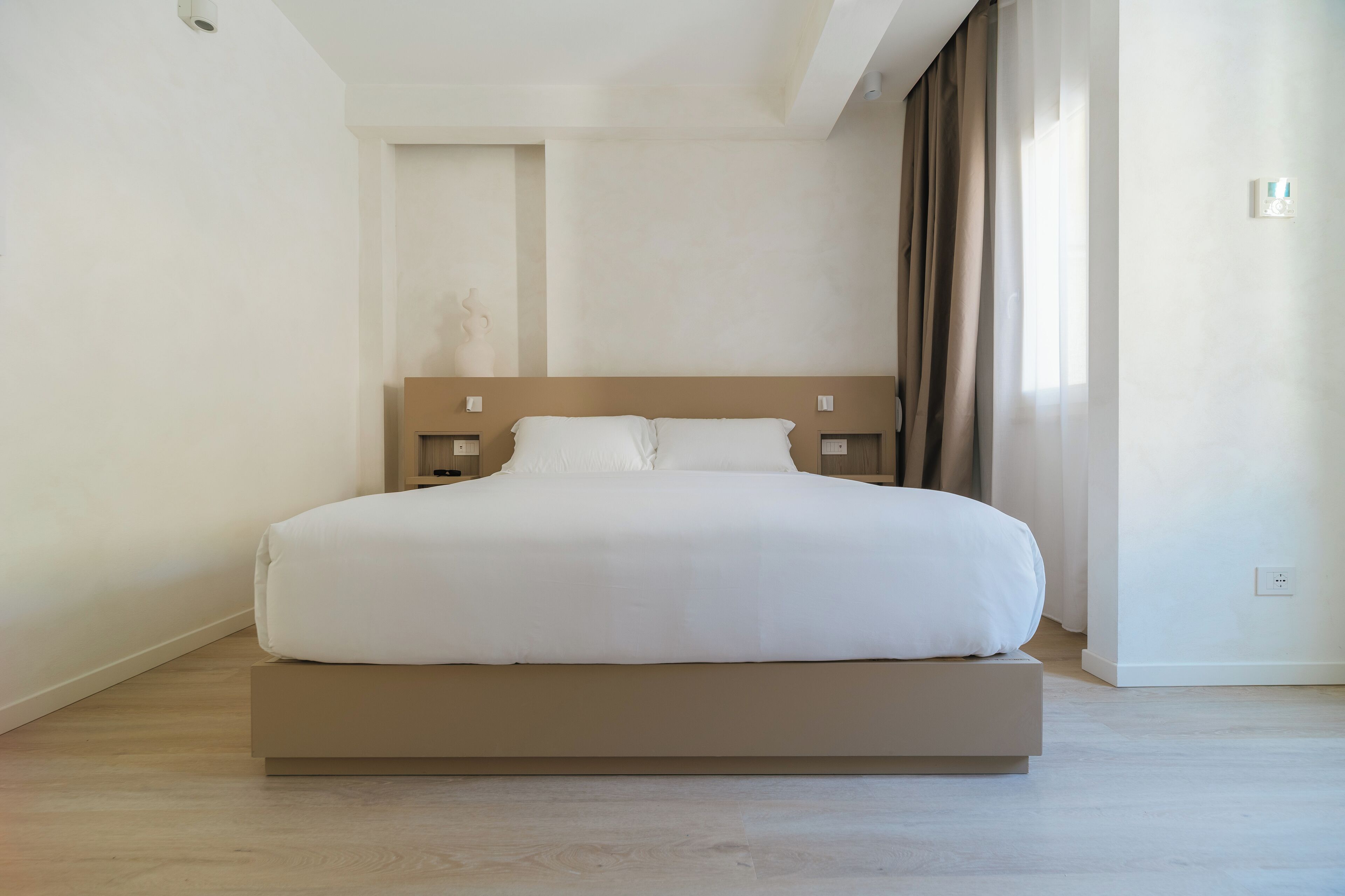 A modern hotel room with a large bed, a wooden headboard, and a neutral color scheme.