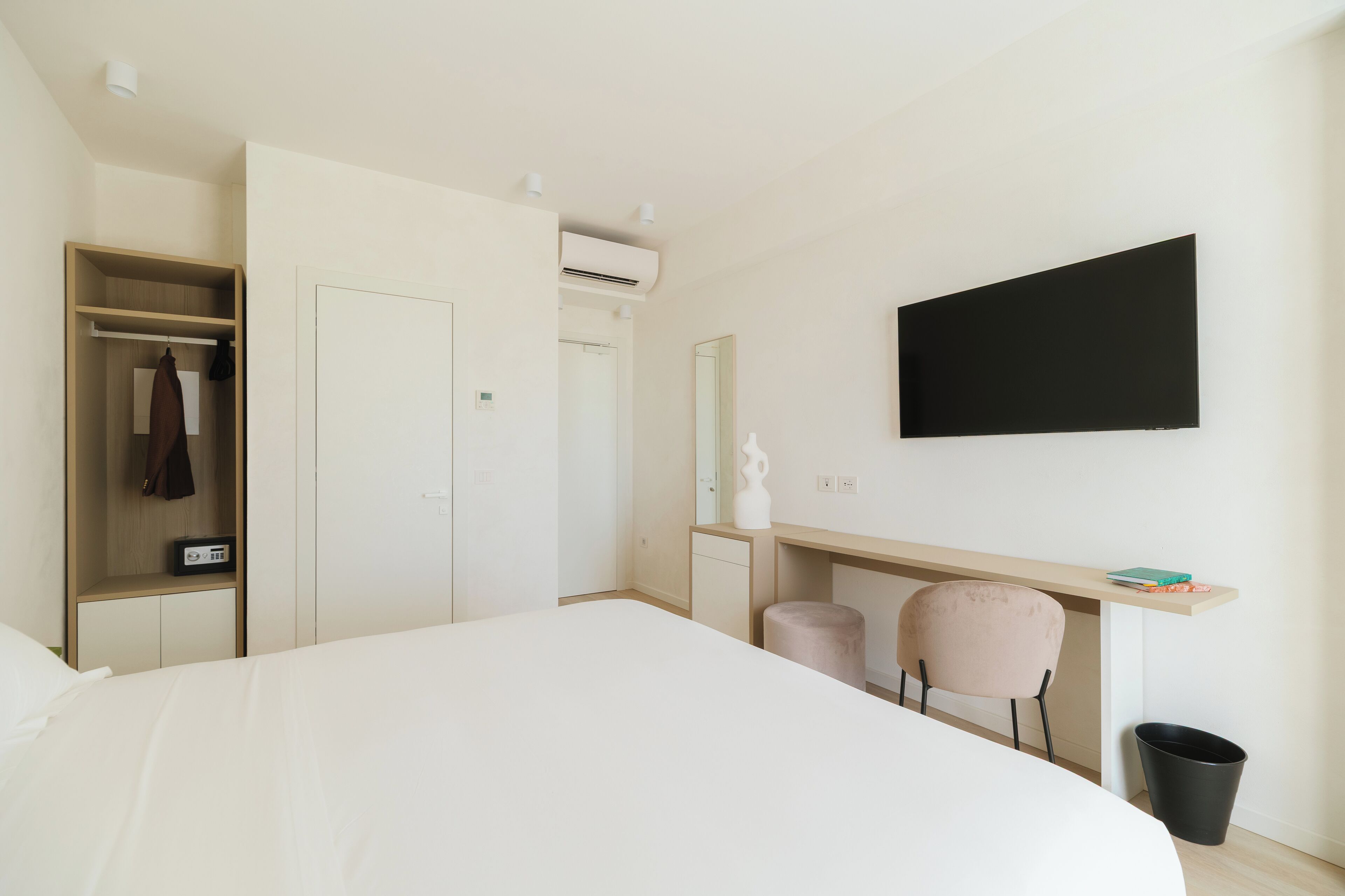 Una moderna camera d'albergo con un grande letto, una scrivania con una sedia, un armadio, uno specchio e una TV a parete.