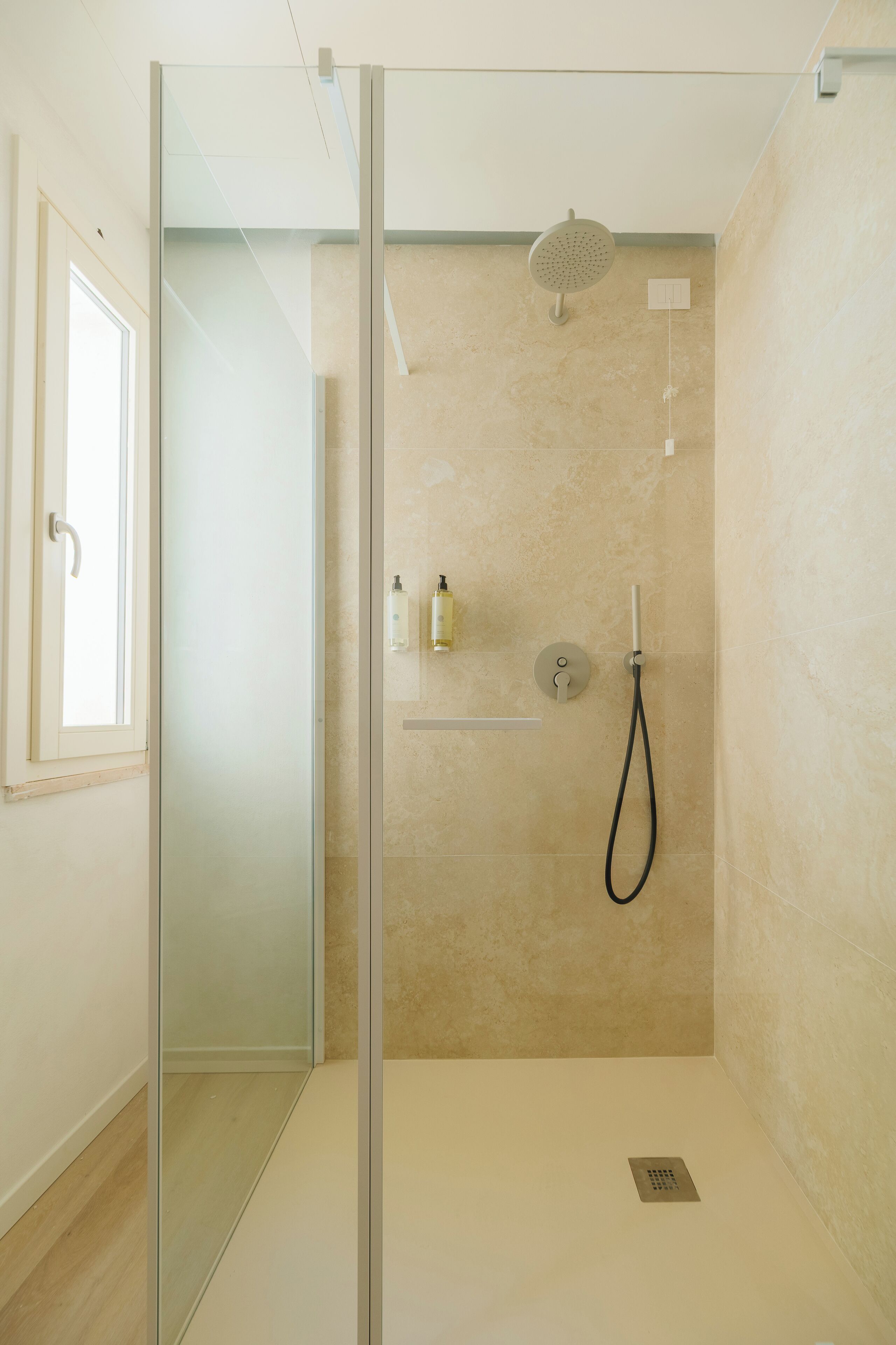 A modern shower with a glass door, a handheld showerhead, and a wall-mounted control panel.