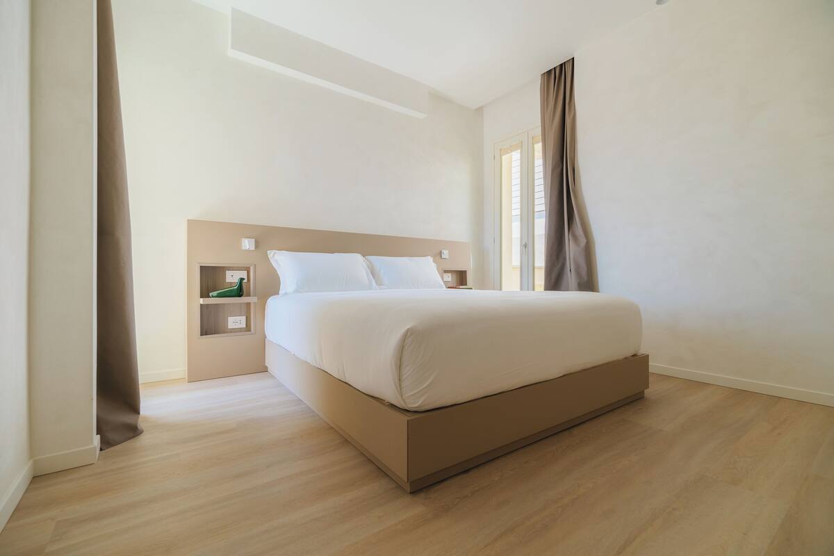 A modern bedroom with a large bed, a bedside table, and a built-in shelf.