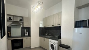 A compact kitchen with a washing machine, a microwave, and a built-in oven. - Charming air-conditioned apartment (Sérignan)