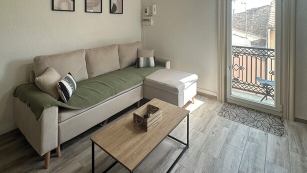 A modern living room with a sofa, a coffee table, and a balcony with a railing. - Charming air-conditioned apartment (Sérignan)