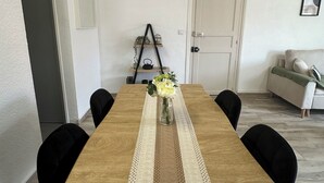 A dining area with a wooden table, a lace table runner, and a vase with flowers. There is a black chair on one side and a white door in the background. - Charming air-conditioned apartment (Sérignan)