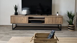 A modern living room with a wooden TV stand, a flat-screen TV, and a small potted plant. - Charming air-conditioned apartment (Sérignan)