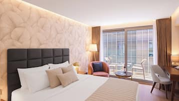 A hotel room with a large bed, a seating area with a chair and table, and a view through a large window.