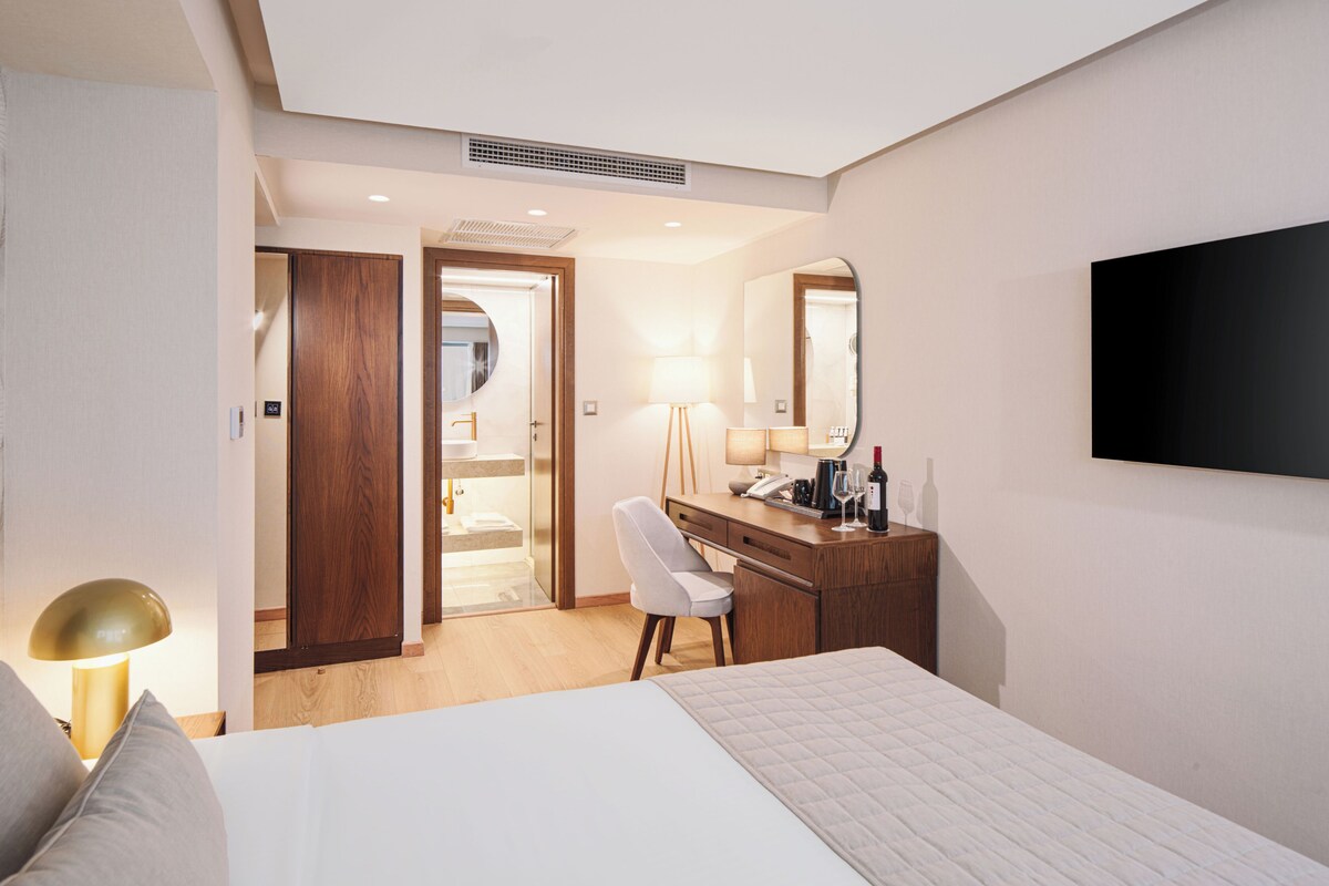 Ein Hotelzimmer mit Bett, Schreibtisch mit Spiegel, Wandfernseher und offenem Badezimmer.