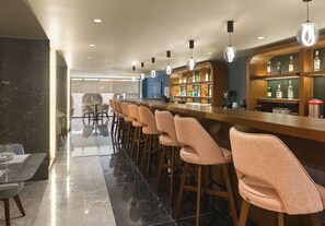 Un espace bar doté d’un long comptoir, de nombreux tabourets et d’une grande variété de bouteilles d’alcool.
