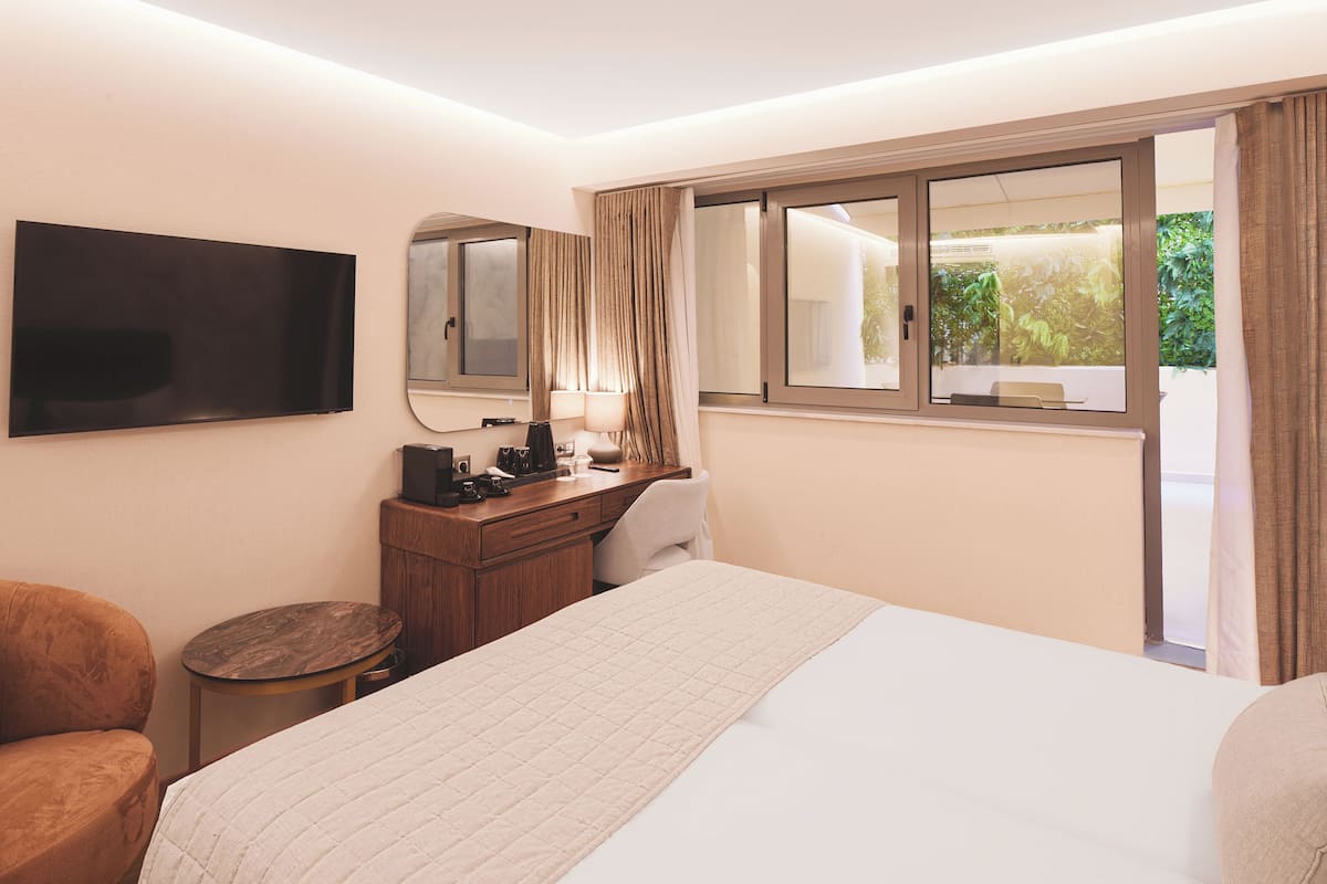 A hotel room with a bed, a desk with a mirror, a television, and a window with curtains.
