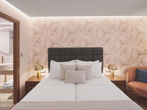 A bedroom with a large bed, two bedside tables with lamps, a wooden nightstand, a chair, and a patterned wall. - Leonardo Hotel Athens City Center (Athens)