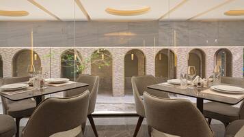 A modern dining area with glass tables and chairs, a brick wall with arches, and a view through a glass partition.