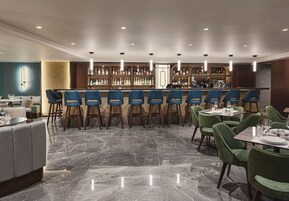 Zona de bar con diversas opciones de asientos, incluyendo taburetes y mesas, y una barra bien surtida.