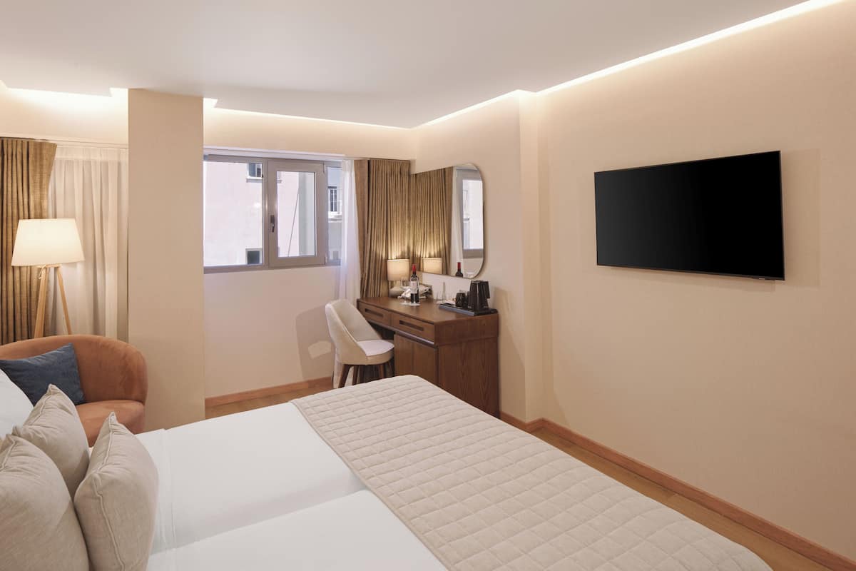 Habitación de hotel con cama, escritorio, silla, televisor y ventana con cortinas.