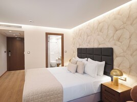 Ett modernt hotellrum med en stor säng, ett sängbord med en lampa, ett trägolv och en vägg med en intressant yta.
