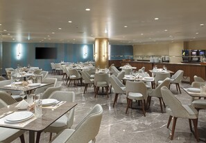 Une salle à manger d’hôtel avec de nombreuses tables et chaises, une grande colonne et un comptoir de buffet.