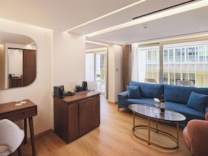 Ein modernes Hotelzimmer mit einem Holztisch, einer Sitzecke, einem Glastisch und einem großen Fenster mit Blick auf die Stadt.