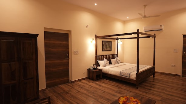 A bedroom with a four-poster bed, wooden flooring, a nightstand, and a bowl of fruit on a table.