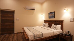 A neatly made bed with a wooden headboard, a bedside table with a kettle, and a wall-mounted air conditioner.