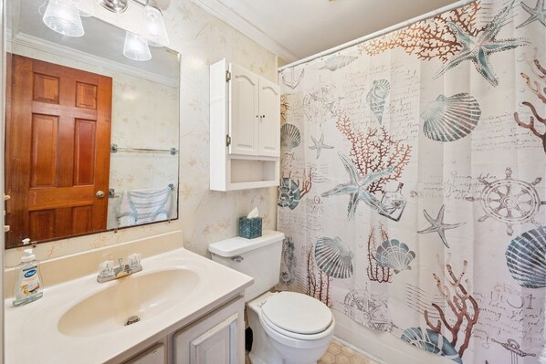 A bathroom with a wooden door, a white sink with a soap dispenser, a toilet, and a shower curtain with a sea-themed design. - Berry Restful 5 Bedroom Home (Georgetown)