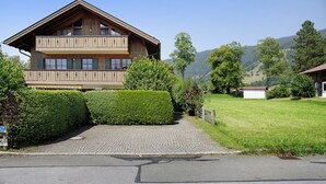 A two-story wooden building with balconies, a paved driveway, and a grassy area with trees.